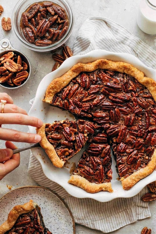 someone slicing pecan pie in a ceramic pie dish plate