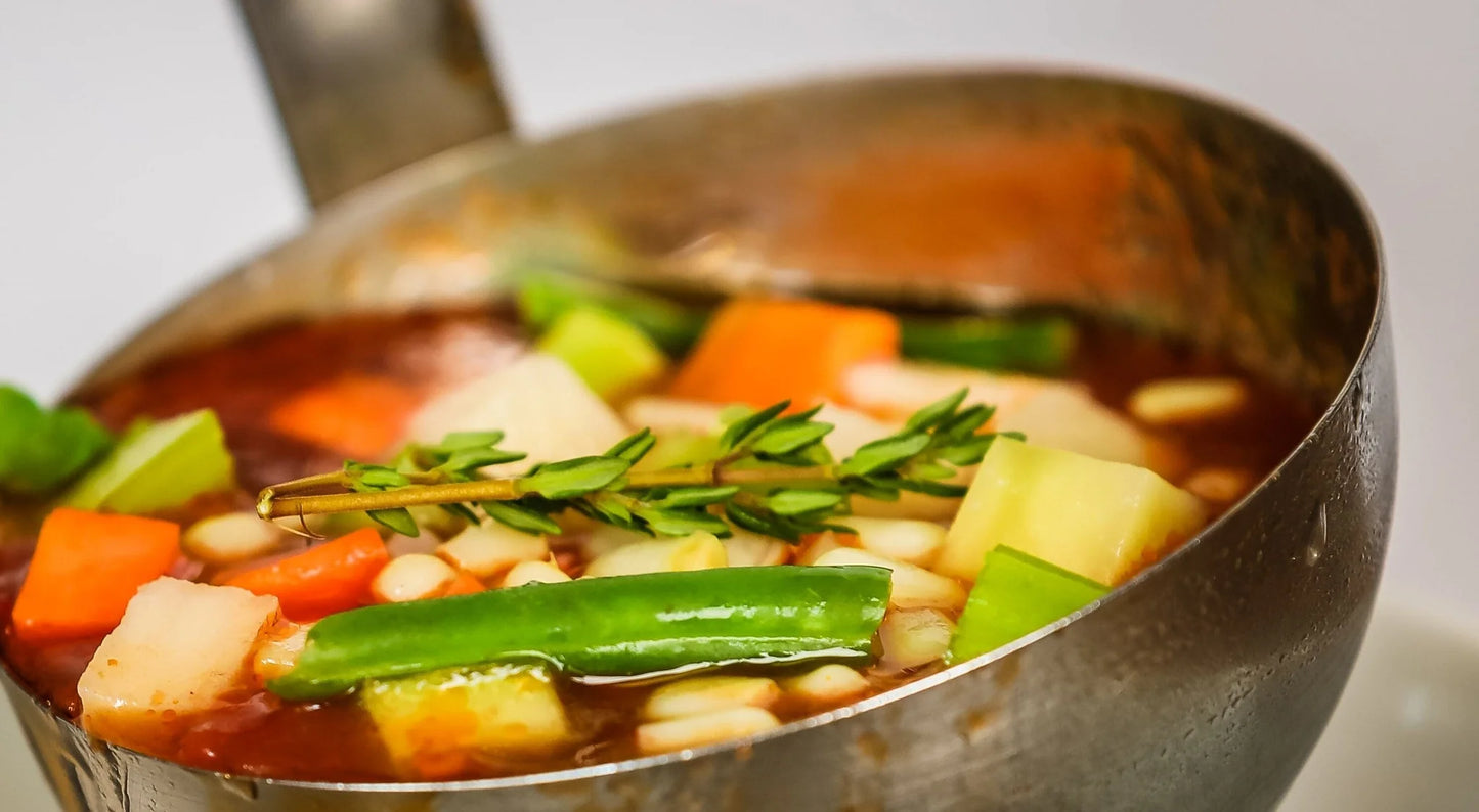 Vegetable soup in a pot with carrots, beans, and greens.