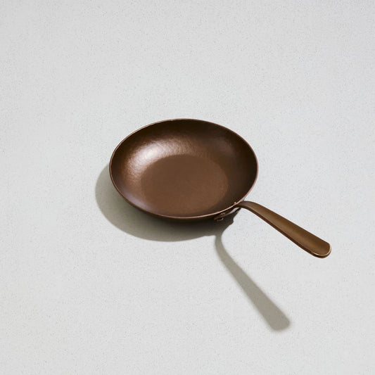 A hand-forged bronze little farmhouse skillet with a long handle, isolated on a white background.
