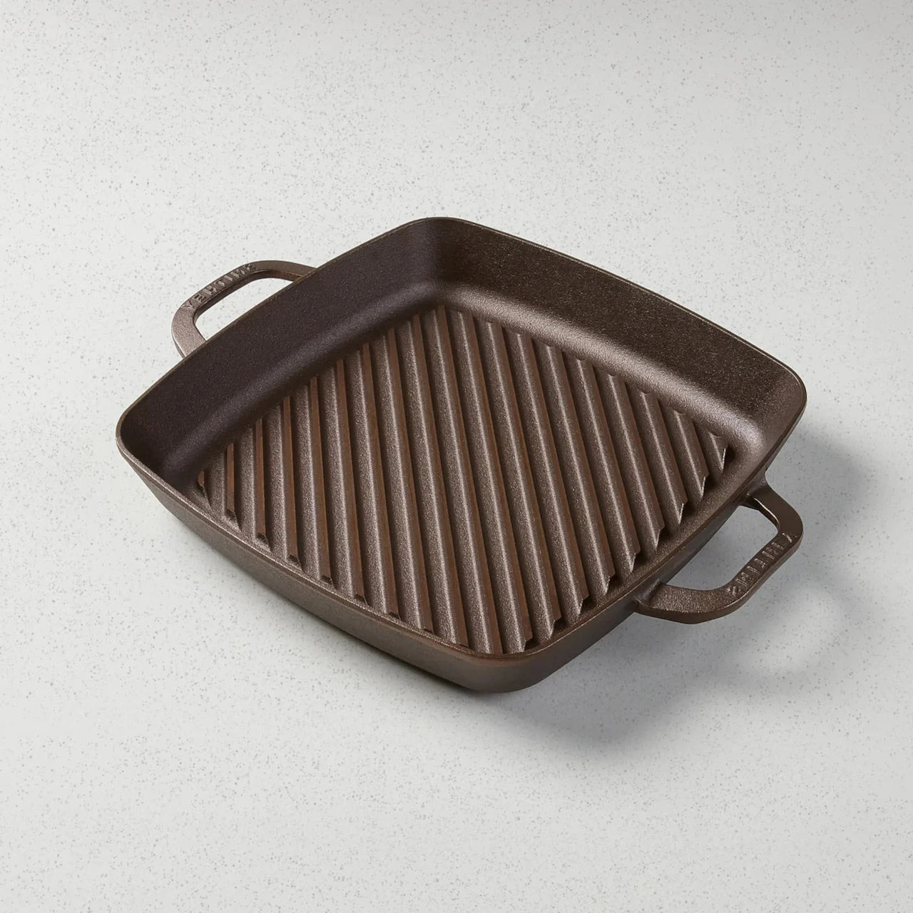 A square, bronze cast iron grill pan with raised interior ridges and two handles.