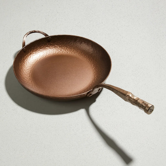 A hand-forged bronze deep farmhouse skillet with a long handle, displayed on a light background.