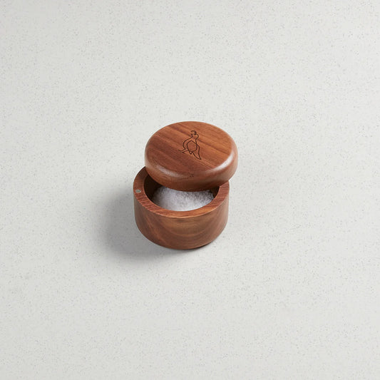 A solid walnut salt keeper with a magnetic rotating lid, partially filled with salt, on a light background.
