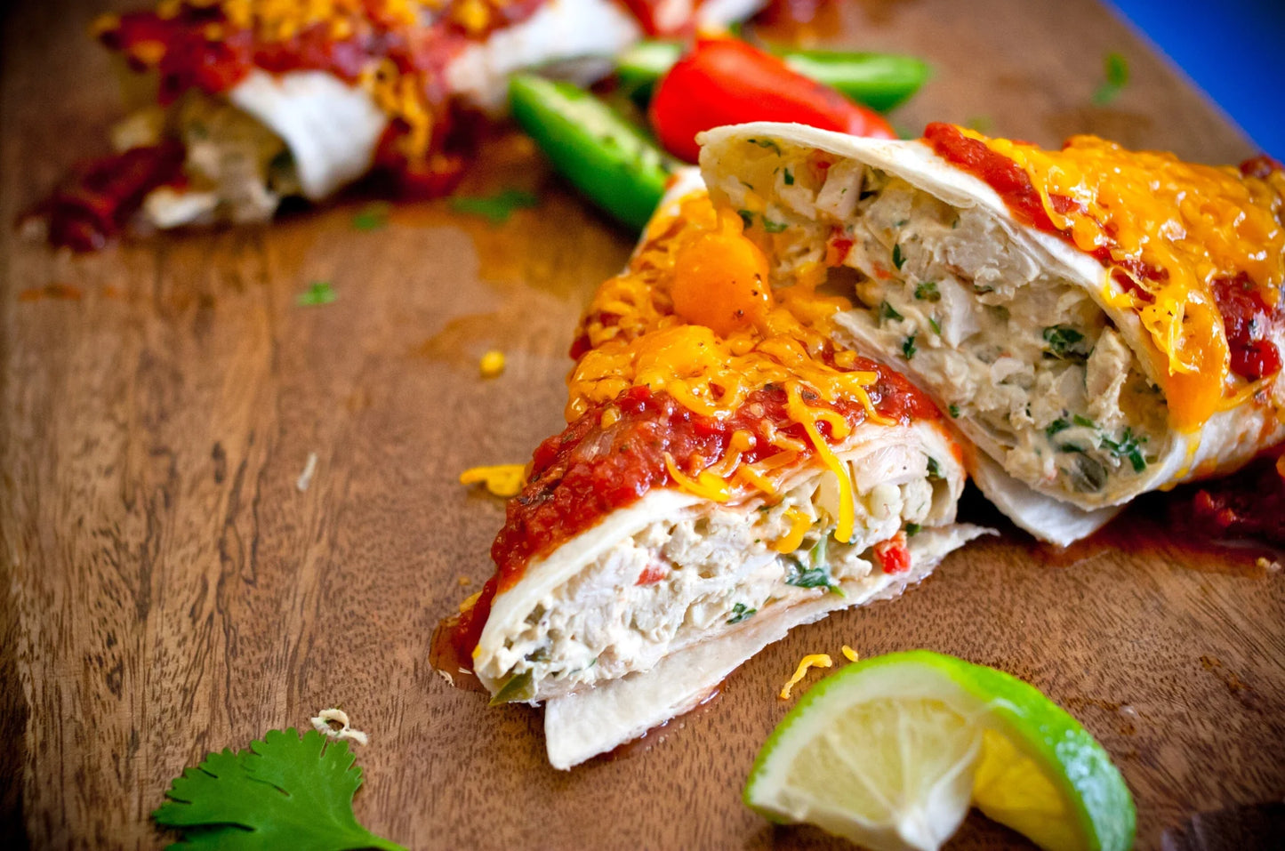 Burrito cut in half on a wooden surface with salsa and lime